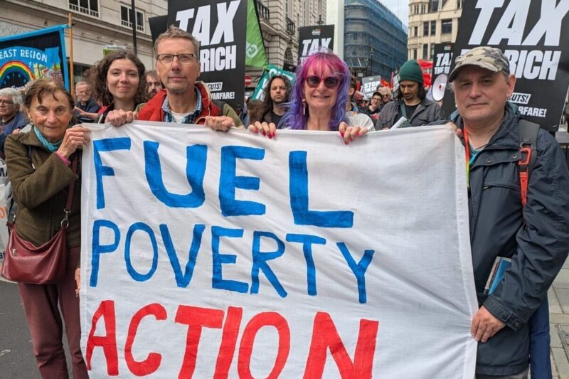 Members and supporters in London hold the FPA banner. Placards in the background read 'tax the rich'