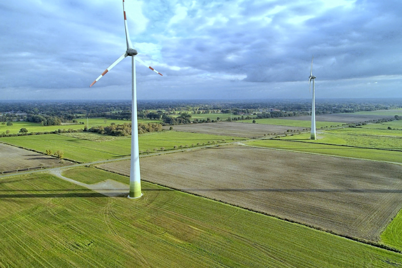 A photograph of two wind turbines in green fields