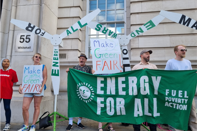 Demonstrators hold banners reading 'Make Green Fair' and 'Energy For All', alongside windturbines bearing these slogans and 'End Oil Wars'.